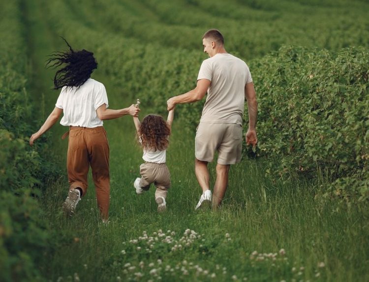 A joyful family strolls through a lush green field, enjoying quality time together.